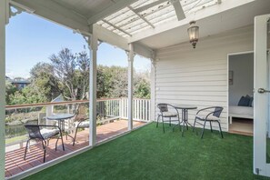 A covered patio with a table and chairs, a door leading to a bedroom, and a view of the surrounding area. - Willow Landing Beach House with Private Jetty (Frankston)