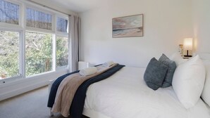 Een slaapkamer met een bed, een raam, een schilderij en een bedlampje.