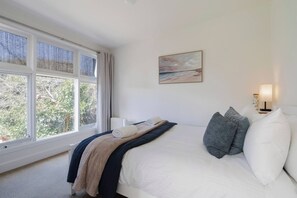 A bedroom with a bed, a window, a painting, and a bedside lamp. - Willow Landing Beach House with Private Jetty (Frankston)