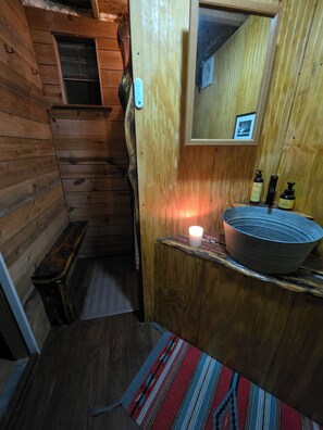 A wooden cabin interior with a bench, a mirror, a sink with a basin, and a candle. - Adventure by day, Stargazing by night , unplug under the Big Bend Stars
 (Terlingua)