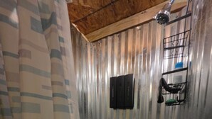 Une douche avec un mur en métal, un pommeau de douche, un porte-serviettes et un drain.