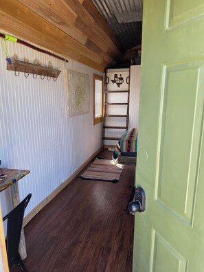 A room with a wooden floor, a bed with a colorful blanket, a ladder, a map on the wall, and a door with a handle. - Adventure by day, Stargazing by night , unplug under the Big Bend Stars
 (Terlingua)