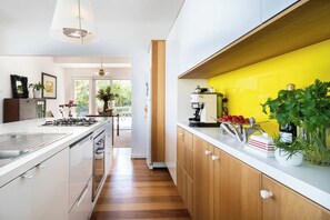 A modern kitchen with white cabinetry, a yellow backsplash, and wooden flooring. - Couples Corner A Stylish Bay View Retreat (McCrae)