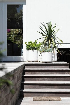 A set of outdoor steps leading to a white building with three potted plants on the landing. - Couples Corner A Stylish Bay View Retreat (McCrae)