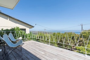A wooden deck with a hanging chair, a white railing, and a view of the ocean. - Couples Corner A Stylish Bay View Retreat (McCrae)