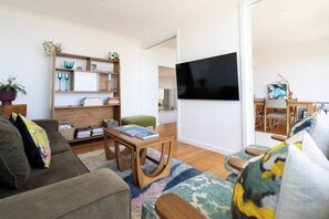 A modern living room with a sofa, coffee table, and bookshelf. A flat-screen TV is mounted on the wall. - Couples Corner A Stylish Bay View Retreat (McCrae)
