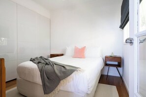 A bedroom with a bed, a nightstand, a window, and a door. - Couples Corner A Stylish Bay View Retreat (McCrae)
