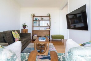 A living room with a sofa, a coffee table, a bookshelf, and a TV mounted on the wall. - Couples Corner A Stylish Bay View Retreat (McCrae)