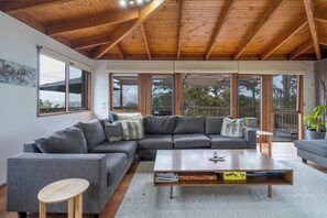 A modern living room with a sectional sofa, a coffee table, and large windows offering views of the outdoors. - McRae Hillside Terrace Panoramic Family Living (McCrae)