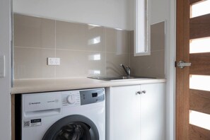 Kompakti pyykinpesutila, jossa on Westinghouse-merkkinen pesukone, pesuallas ja kaappi.