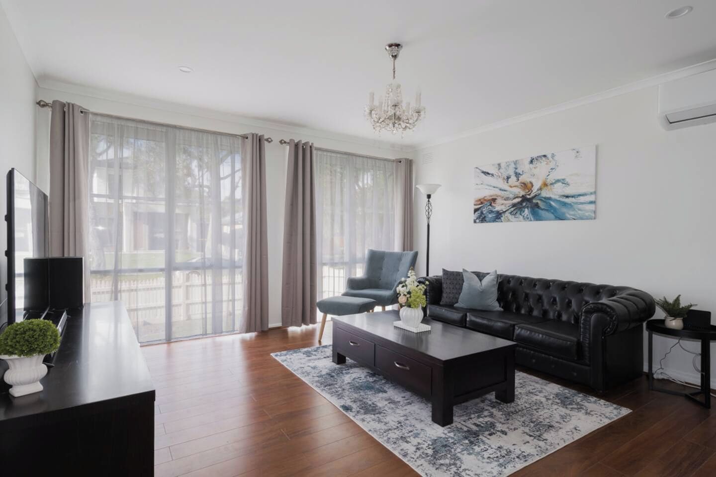 Un salon moderne avec un canapé en cuir noir, une table basse et une grande fenêtre avec des rideaux.