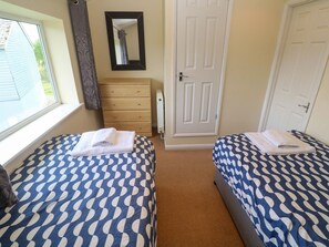A bedroom with two beds, a dresser, a mirror, and a door. - 87 Atlantic Reach (St. Columb Major)