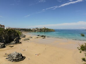 A coastal beach with rocky outcrops, a sandy shore, and buildings on a cliff. - 87 Atlantic Reach (St. Columb Major)