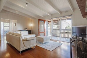 Ein geräumiges Wohnzimmer mit einer Couch, einem Couchtisch und einem Fernseher. Eine Glastür führt auf eine Terrasse.