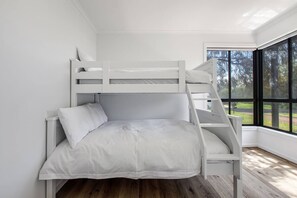 A bunk bed with a ladder, white bedding, and a large window with a view of trees. - Hearthstone Haven Spacious Beachside Group Getaway (Safety Beach)