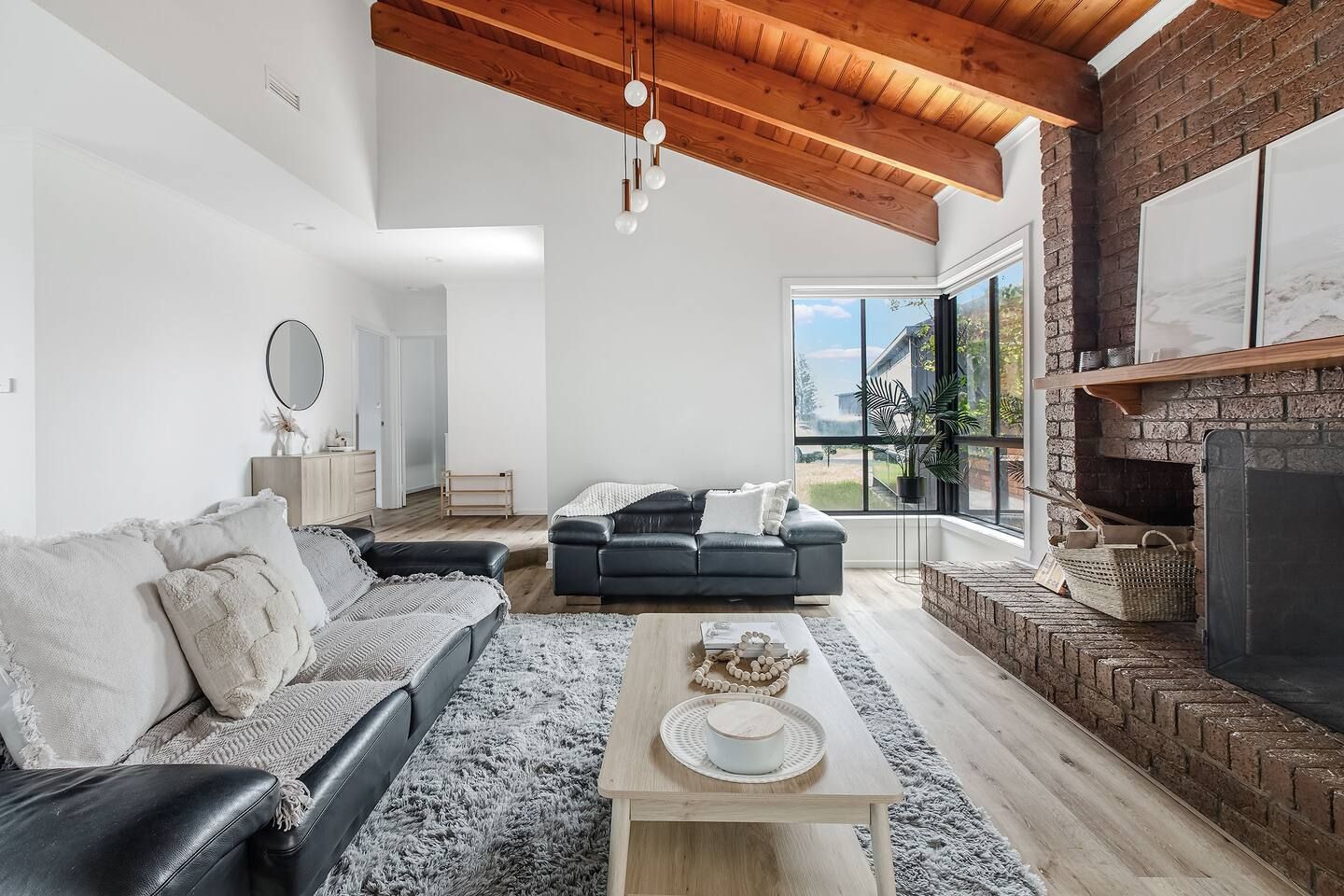 A modern living room with a fireplace, a sofa set, a coffee table, and a large window offering a view of the outdoors.