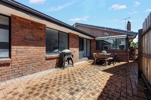 A brick house with a patio, a barbecue grill, and a dining table with chairs. - Hearthstone Haven Spacious Beachside Group Getaway (Safety Beach)