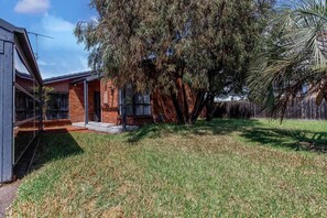 A residential property with a brick house, a lawn, and a large tree. - Hearthstone Haven Spacious Beachside Group Getaway (Safety Beach)