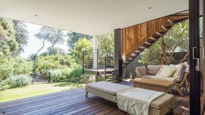A modern outdoor deck with a wooden floor, a wicker sofa, and a staircase. - Ti Tree House Live like a Bonbeach Local (Bonbeach)
