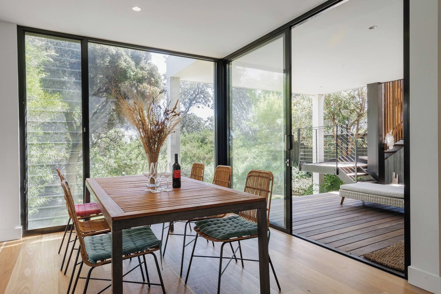 A dining area with a wooden table, wicker chairs, and a bottle of wine.