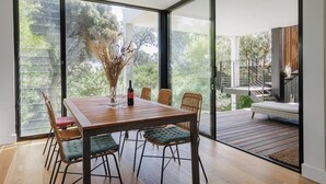 Un comedor con una mesa de madera, sillas de mimbre y una botella de vino.