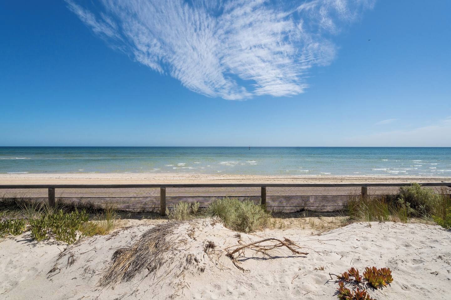 A beach with a wooden fence, sandy dunes, and a clear blue sky.