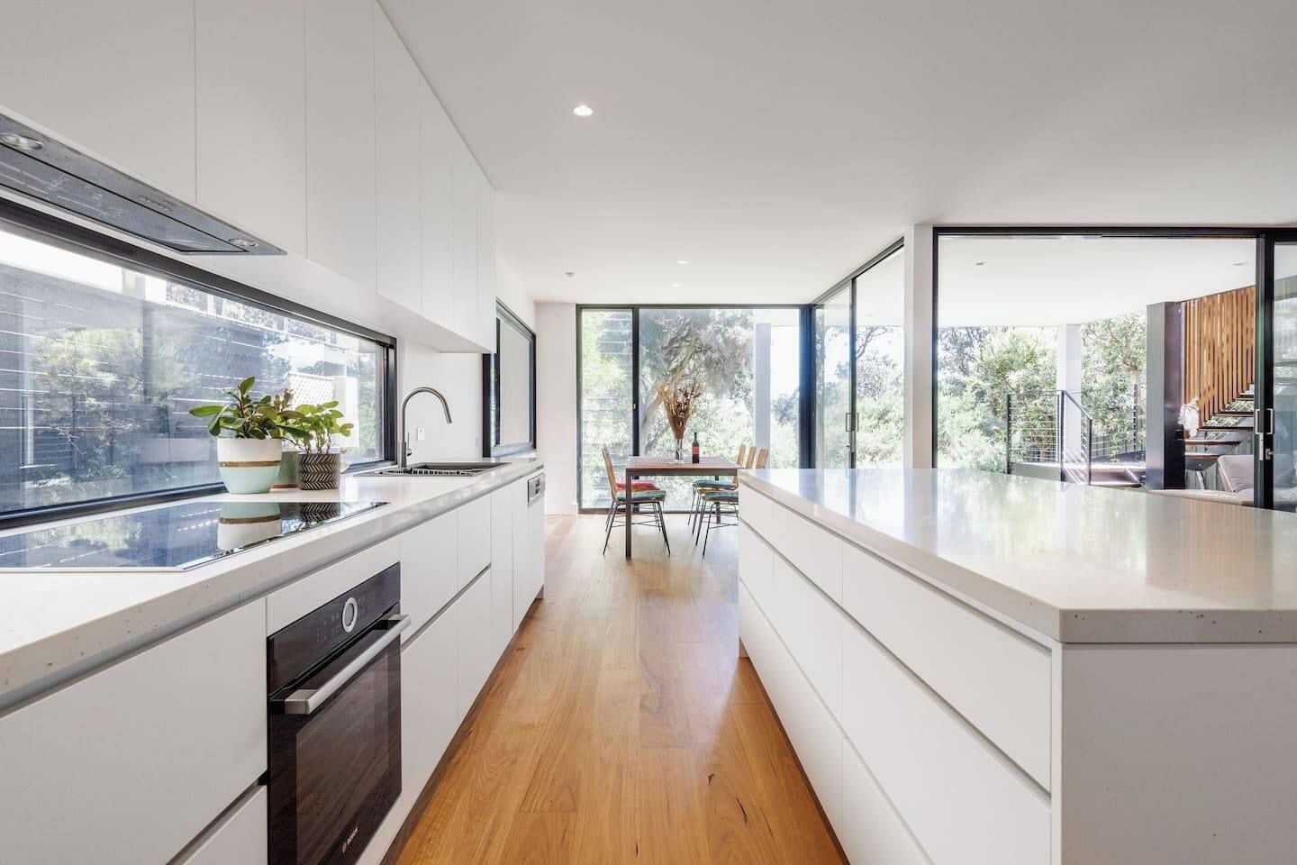 A modern kitchen with a central island, a dining area with a table and chairs, and large windows providing natural light and views.