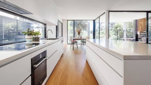 Una cocina moderna con una isla central, un área de comedor con mesa y sillas, y ventanas amplias que ofrecen luz natural y vistas.