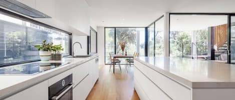 A modern kitchen with a central island, a dining area with a table and chairs, and large windows providing natural light and views.