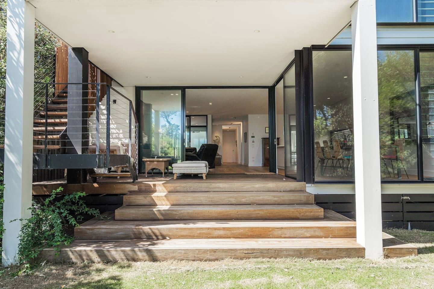 A modern house with a wooden staircase leading to a glass door entrance.