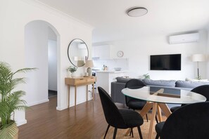 A modern living room with a glass dining table, black chairs, a grey sofa, and a flat-screen TV mounted on the wall. - Bayside Basking Coastal Rye Living at its Best (Rye)