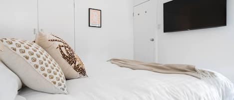 Una camera da letto con un letto, un'opera d'arte incorniciata e una TV a schermo piatto fissata al muro.