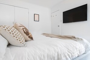 A bedroom with a bed, a framed artwork, and a flat-screen TV mounted on the wall. - Bayside Basking Coastal Rye Living at its Best (Rye)