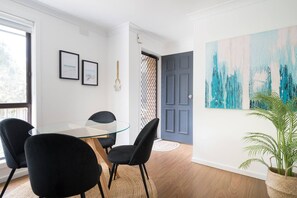 A modern dining area with a glass table, black chairs, and a blue door. - Bayside Basking Coastal Rye Living at its Best (Rye)