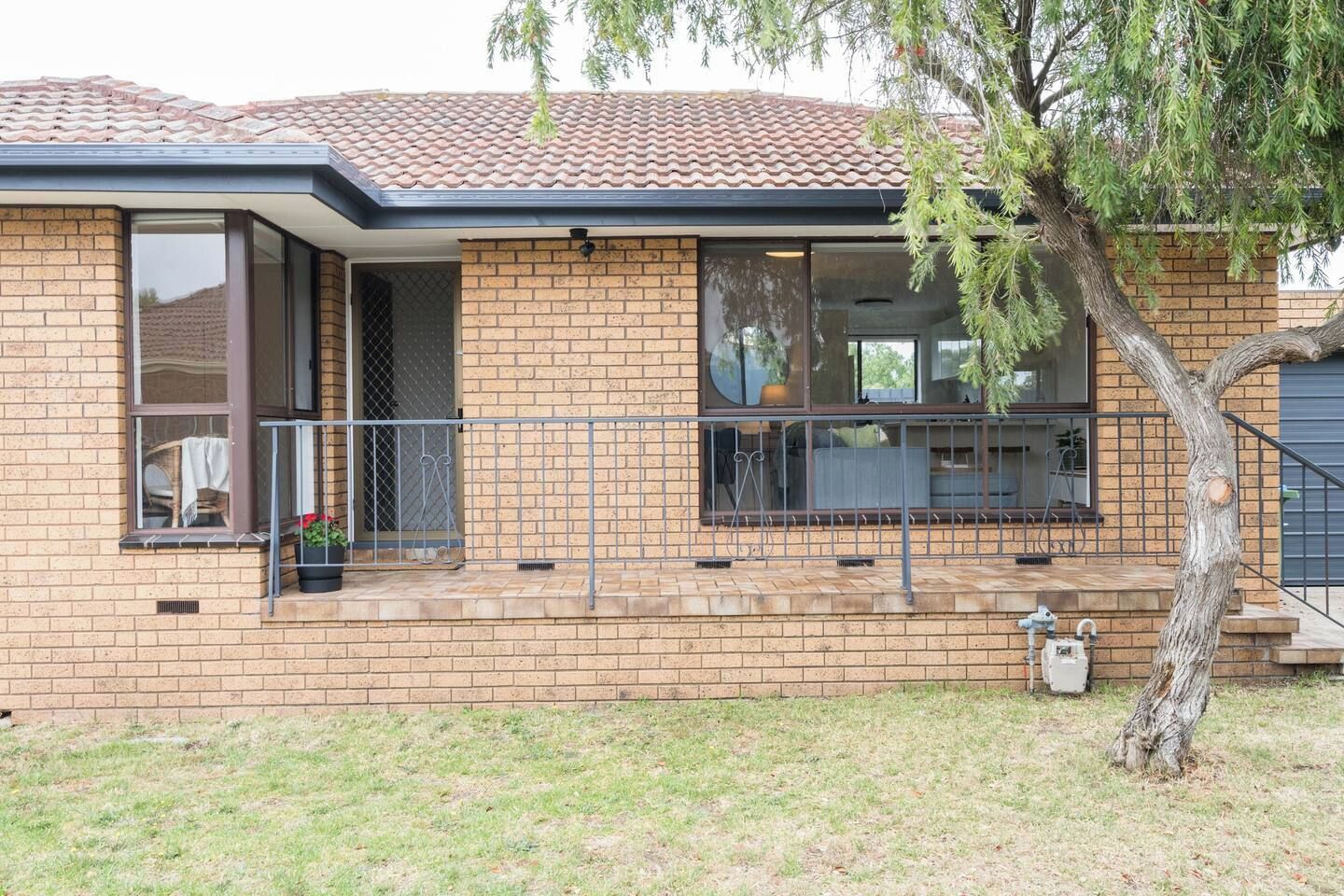 A residential building with a brick facade, a tiled roof, and a small porch area with a railing.