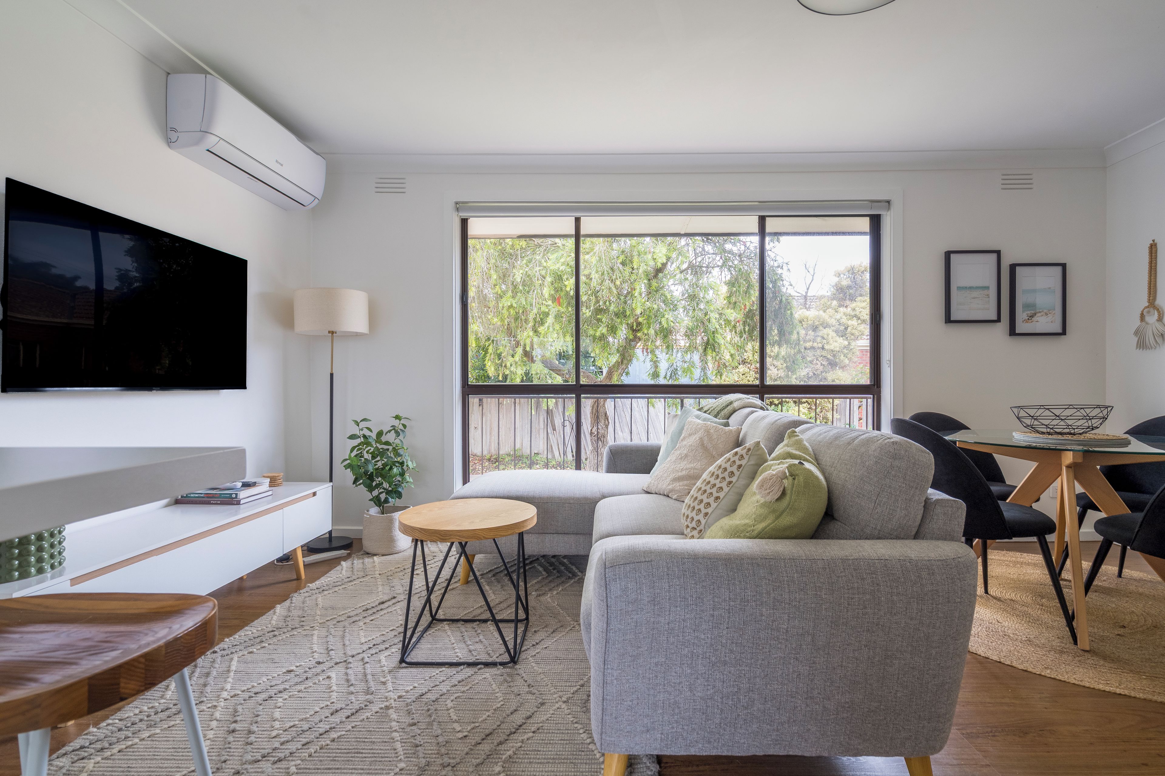 A modern living room with a grey sofa, a round wooden coffee table, and a flat-screen TV mounted on the wall.