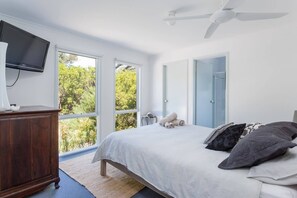 A bedroom with a bed, a TV, a ceiling fan, and large windows. - Stroll to the Sea Sun drenched Seaside Lifestyle (Rye)