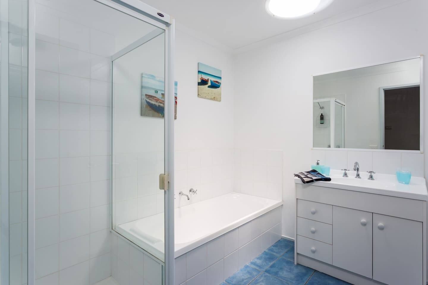A modern bathroom with a glass shower enclosure, a white bathtub, and a vanity with a mirror.