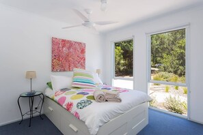 Une chambre à coucher avec un lit, un ventilateur de plafond, une fenêtre et un tableau accroché au mur.