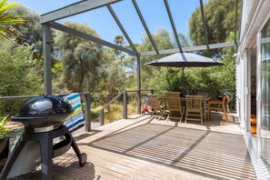 Une terrasse couverte équipée d’un barbecue, de chaises en bois et d’une table.