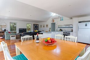 Une cuisine moderne avec des meubles blancs, une table à manger avec des chaises et un coin salon avec un canapé et un téléviseur.