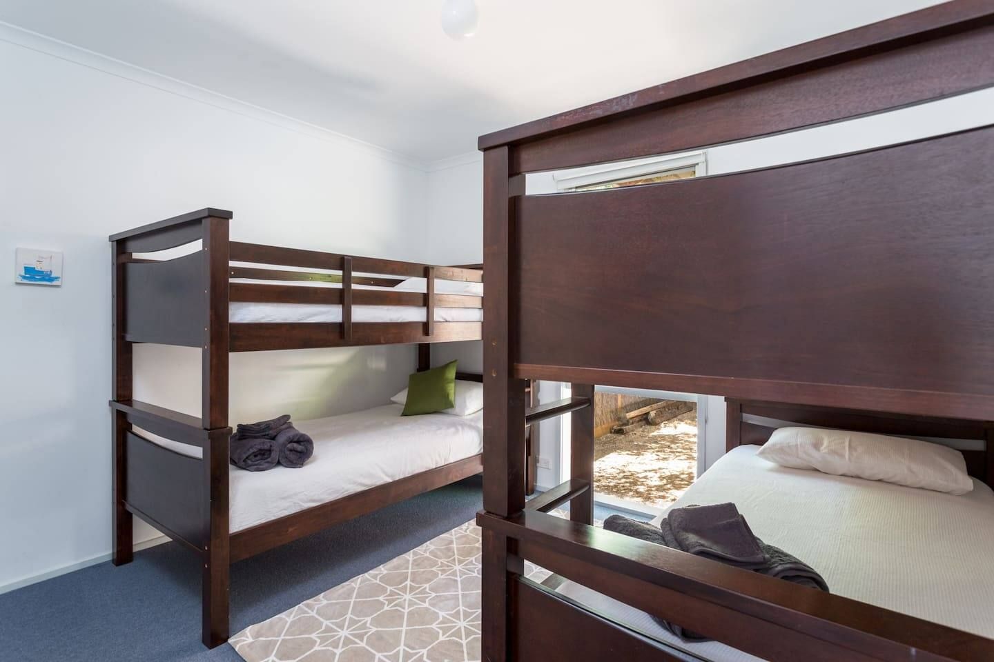A bunk bed room with a window, a small rug, and a picture on the wall.