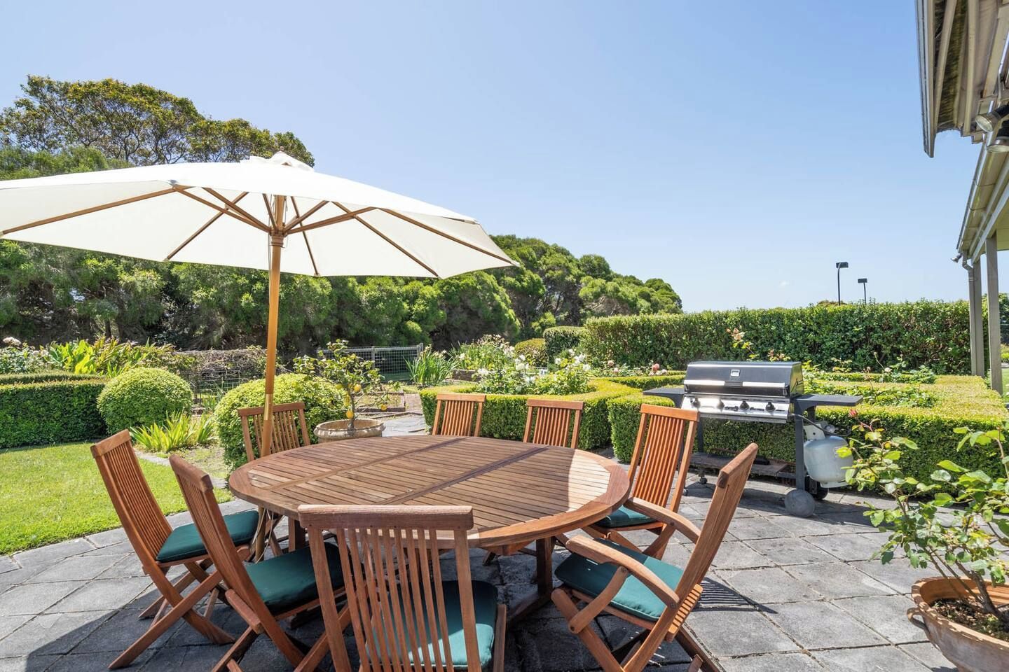 A patio with a round wooden table and chairs, a grill, and a large umbrella.