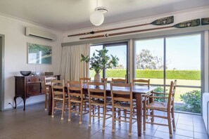 A dining area with a large table and chairs, a vase with greenery, and a view through large windows. - Viewbank Homestead A Sprawling Garden Estate (Shoreham)