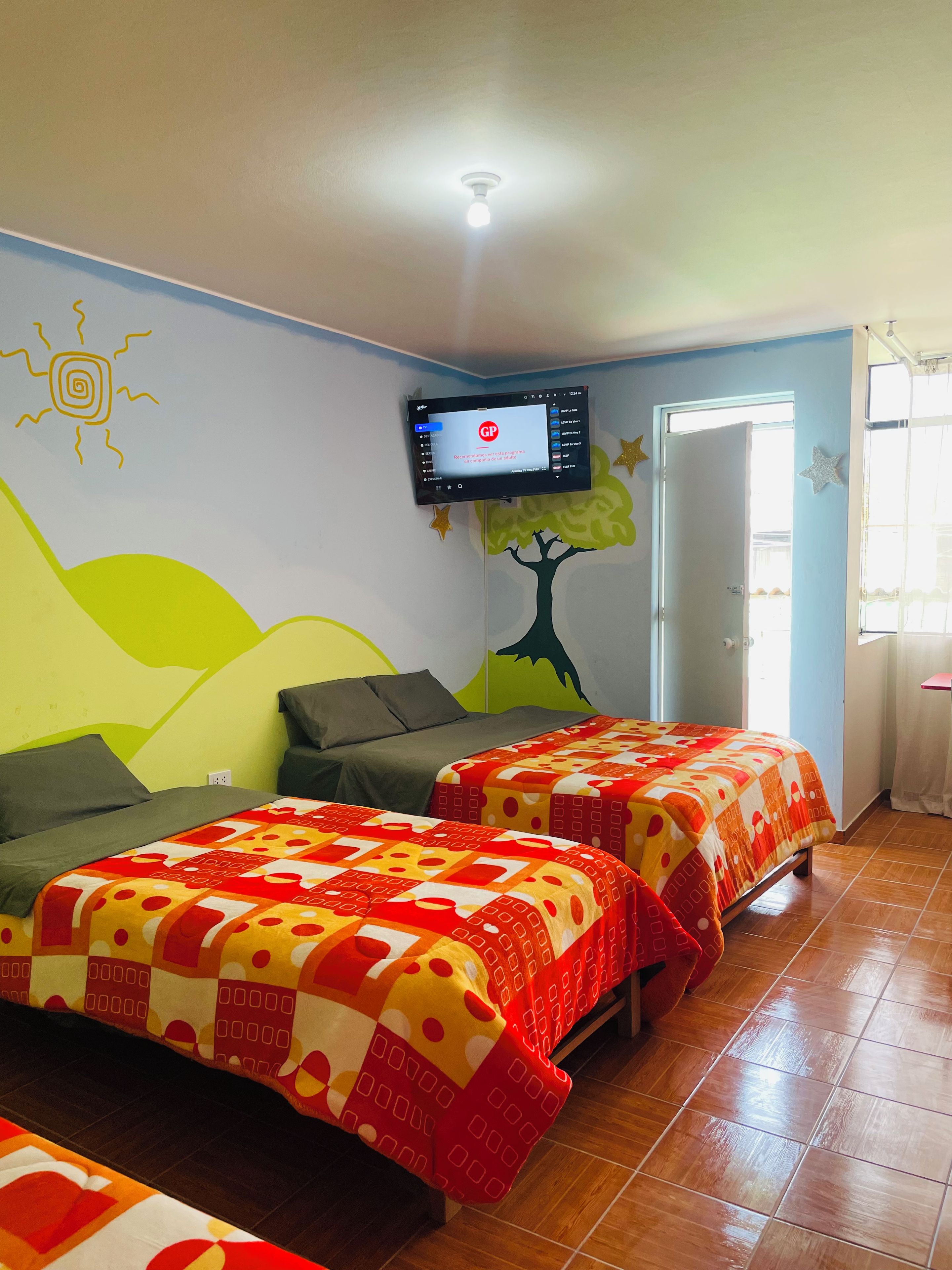 Una habitación con dos camas, un televisor montado y una puerta.