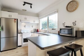 Een moderne keuken met witte kasten, een roestvrijstalen koelkast, een magnetron en een groot raam dat voor natuurlijk licht zorgt.
