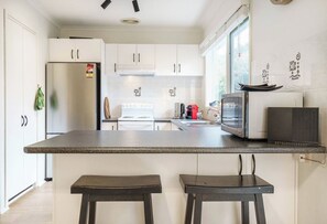 Una cucina moderna con mobili bianchi, un piano di lavoro in granito, un fornello, un forno a microonde e due sgabelli da bar.