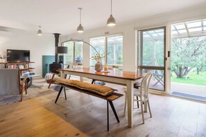 A spacious living area with a wooden dining table, bench, and a television on a stand. - Koonya Keeper Family Living by the Coast (Sorrento)