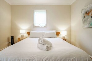 Ein Hotelzimmer mit einem großen Bett, zwei Nachttischlampen, einem Fenster und einem Bild an der Wand.