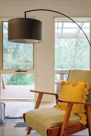 A room with a wooden chair with a yellow cushion, a black lamp, and large windows with a view of greenery. - Koonya Keeper Family Living by the Coast (Sorrento)